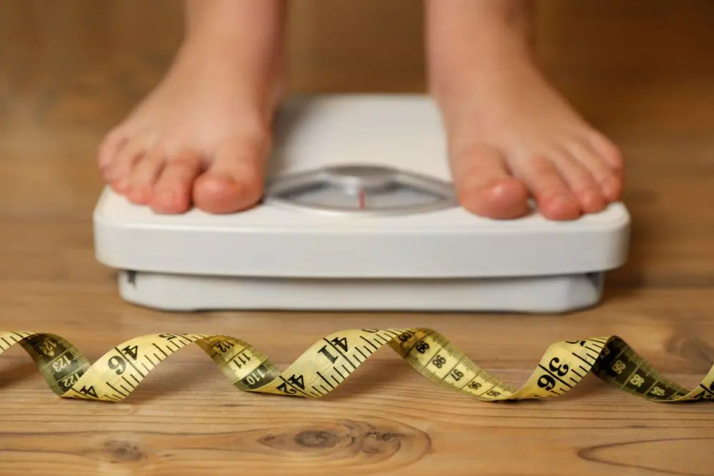 overweight-girl-using-scales-near-measuring-tape-on-wooden-floor-selective-focus