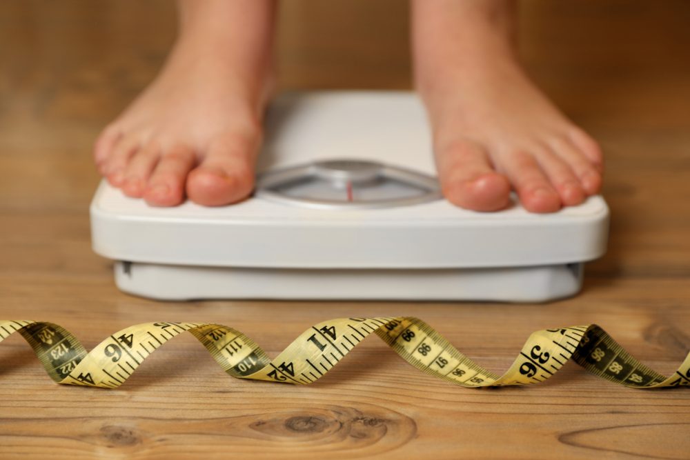 overweight-girl-using-scales-near-measuring-tape-on-wooden-floor-selective-focus